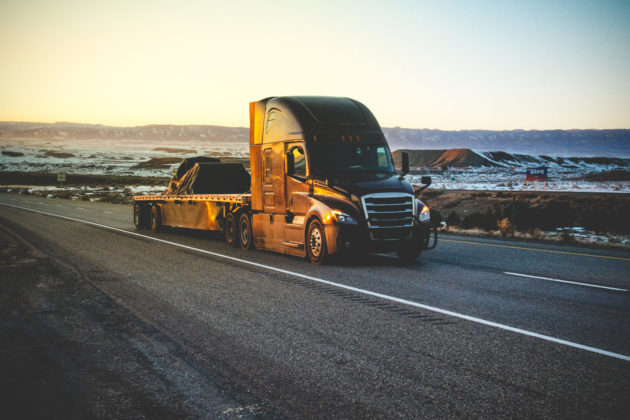 Long Haul Semi Truck Speeding Down Highway In A Snowy Desert Landscape alternate text for this image