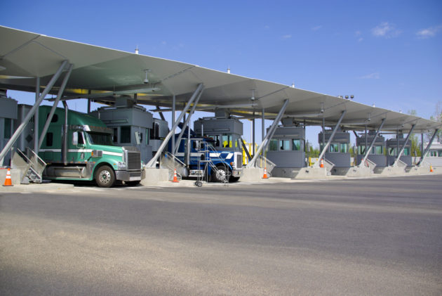 Semi trucks pay at tollbooth at Canadian border alternate text for this image
