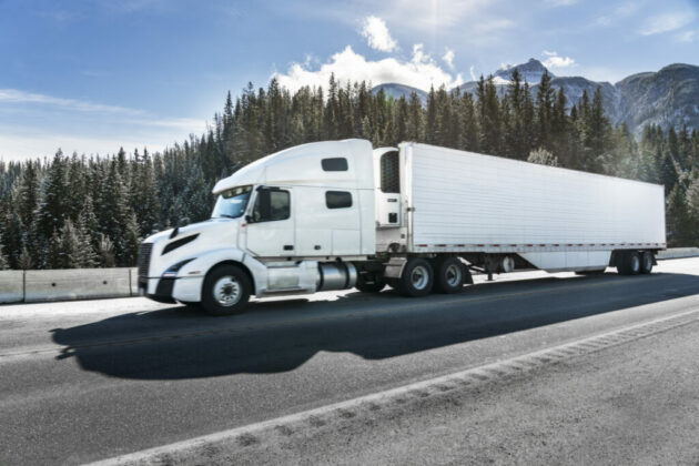 a white semi-truck driving on mountain road alternate text for this image