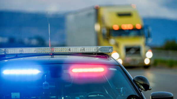 A Highway Patrol Car With The Lights On, Pulling A Driver Over For Speeding As A Semi Truck Drives Passed alternate text for this image