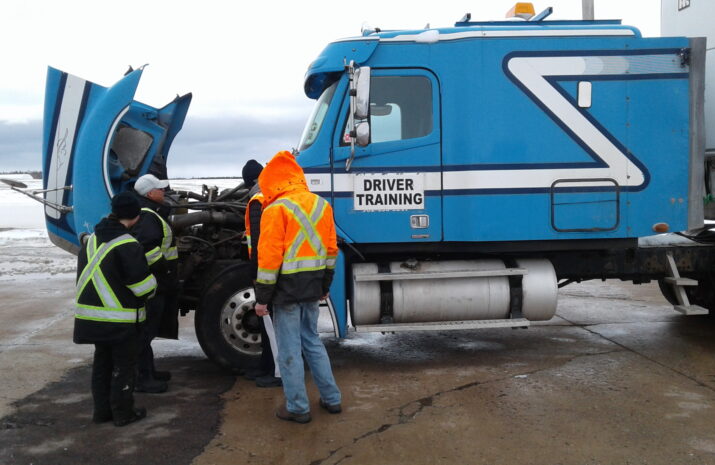 People standing in front of a truck with an open hood.