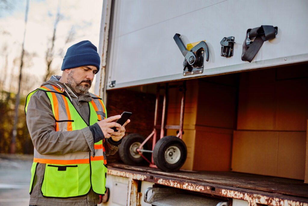 Mid adult courier using mobile phone while closing his truck and preparing for delivery.