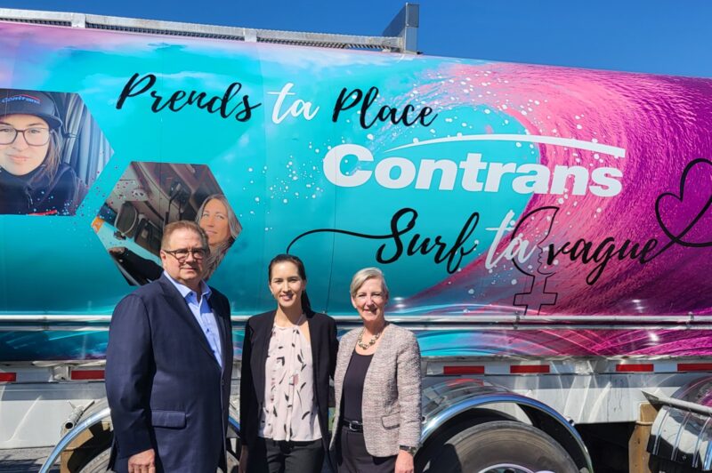 Three people standing in front of a colorful tanker.