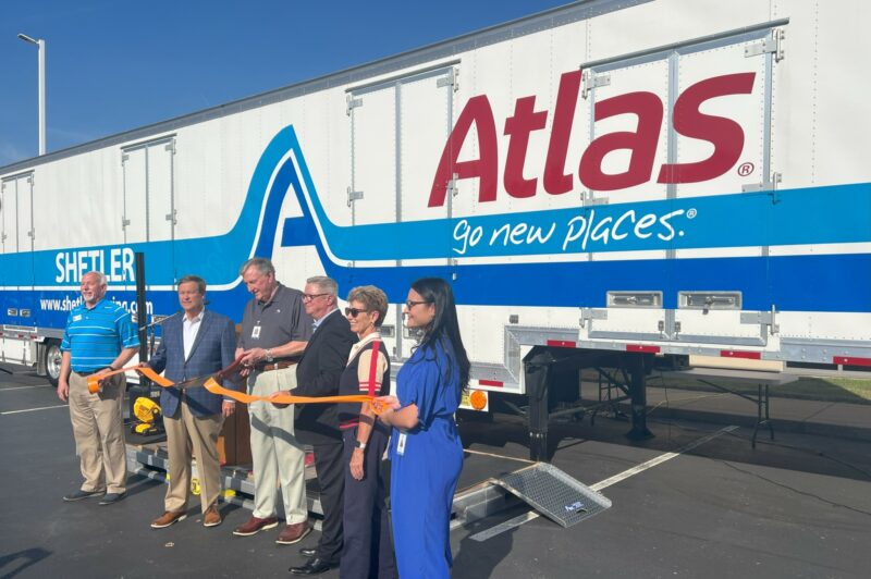 People cut a ribbon in front of a trailer