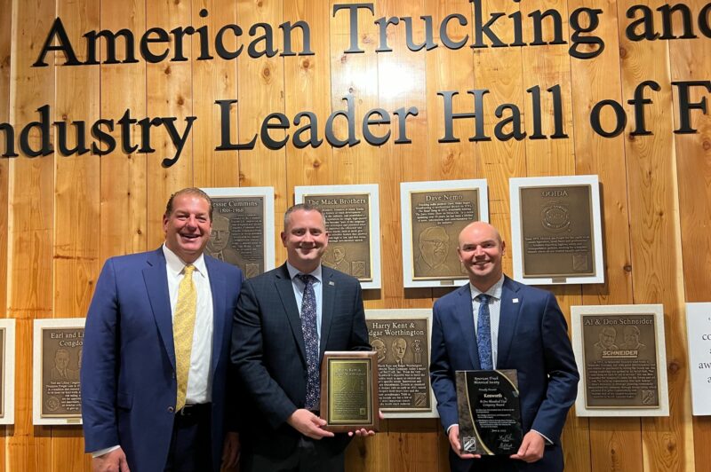 Three men standing in front of a wall filled with plaques