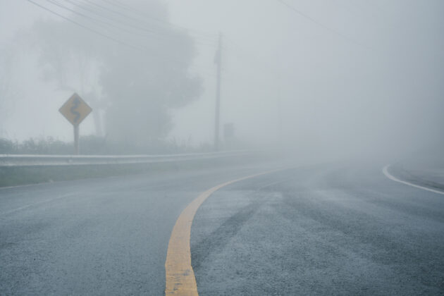 foggy rural asphalt highway perspective with white line, misty road, Road with traffic and heavy fog, bad weather driving alternate text for this image