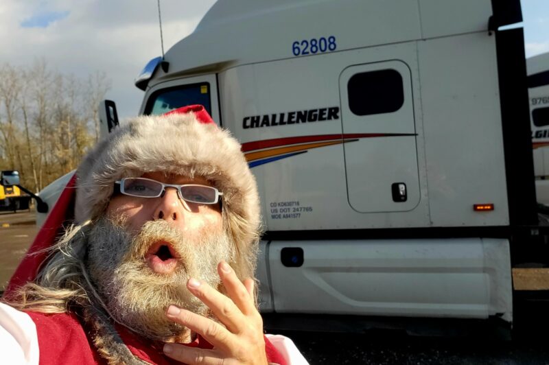 The photo is a selfie of Dave Bennison, a truck driver, dressed as Santa Clause in front of a Challenger truck