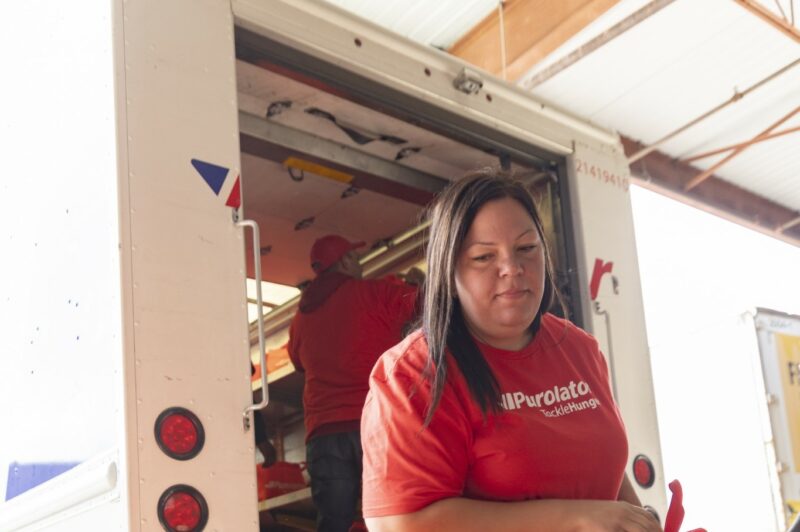 The image is of a women, a team member of Purolator Tackle Hunger, delivering food to the food bank