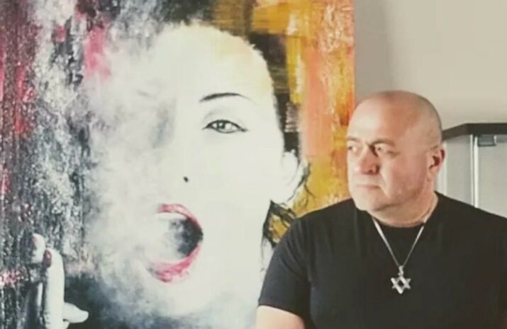 This is a headshot of Eugene Kabrun standing in front of his painting called Passionate Smoker