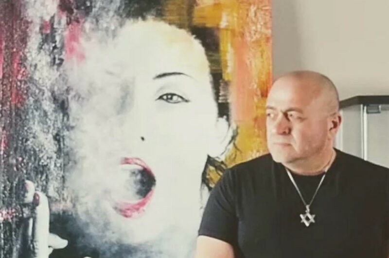 This is a headshot of Eugene Kabrun standing in front of his painting called Passionate Smoker