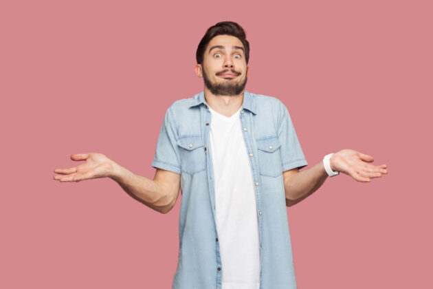 I don’t know. Portrait of confused handsome bearded young man in blue casual style shirt standing with raised arms and looking at camera with answer. alternate text for this image