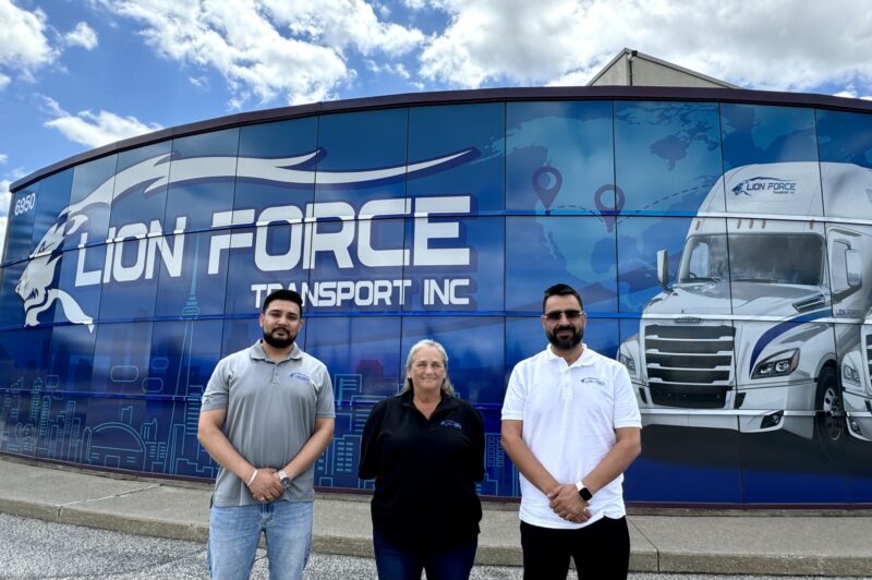 Lion Force's two owners and a general manager outside of the headquarters in Mississauga, Ont, in front of the banner with the logo
