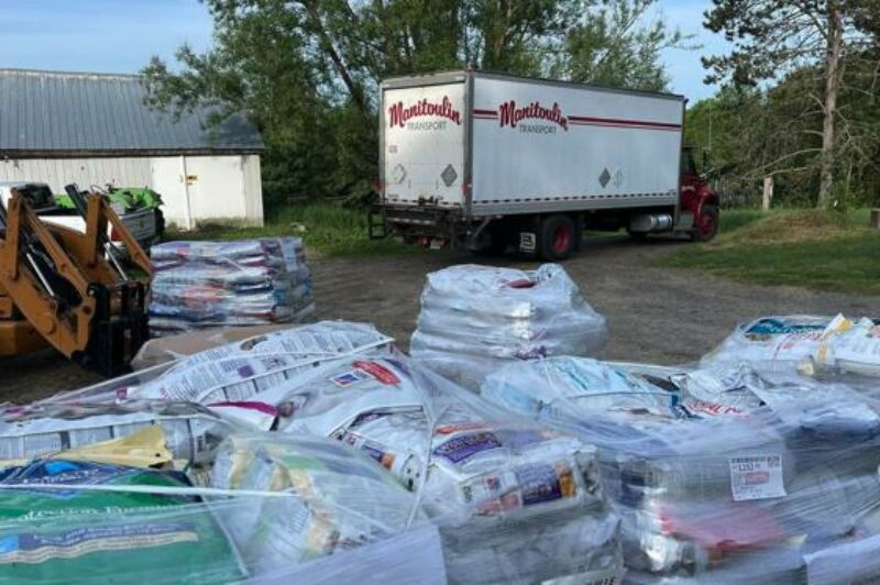 image shows a Manitoulin truck parked near large stacks of bagged items in an outdoor area