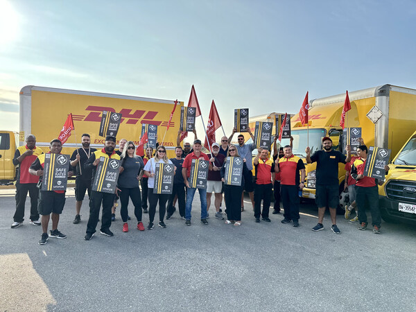 Unifor members holding signs and flags stands in front of DHL-branded trucks, at a organized rally in Hamilton.