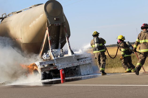 Three fireman rush to put out a brake fire on a semi-truck alternate text for this image