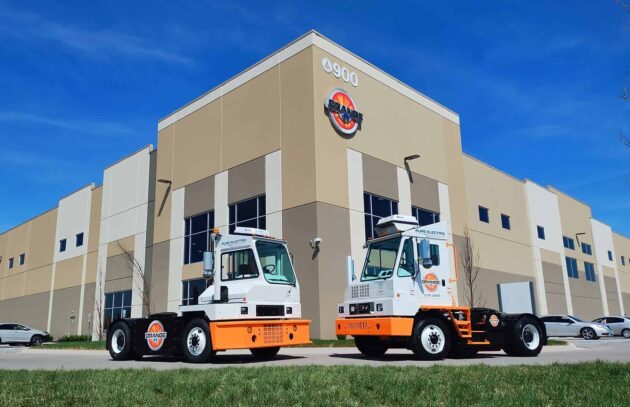 Two orange EV trucks in front on the facility
