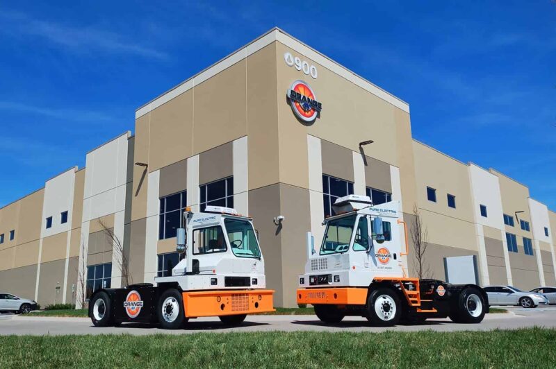 Two orange EV trucks in front on the facility