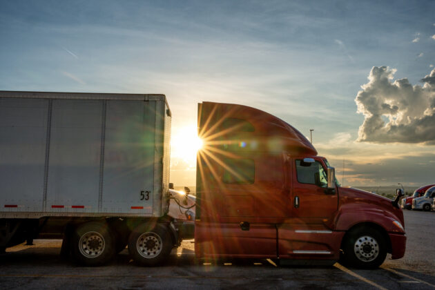 Red Colored Semi-Truck Speeding on a Two-Lane Highway with Cars in Background Under a Stunning Sunset in the American Southwest alternate text for this image