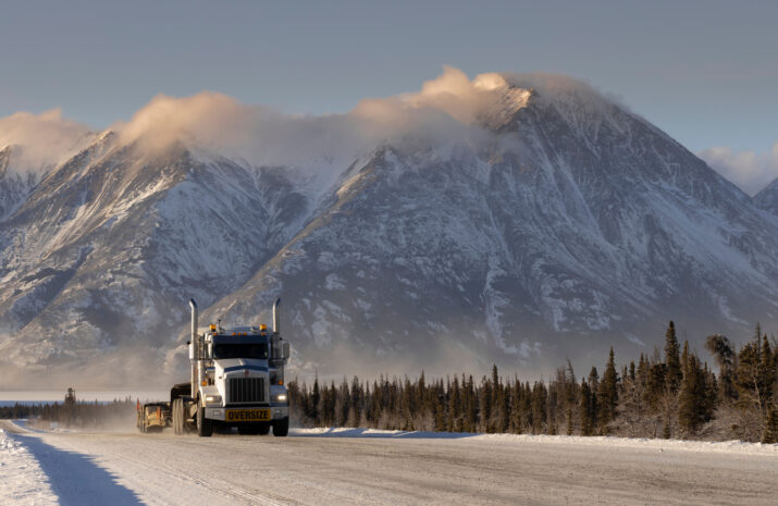 An oversize load truck in the road with forests and snowy mountains in the background in Whitehorse, Yukon, Canada