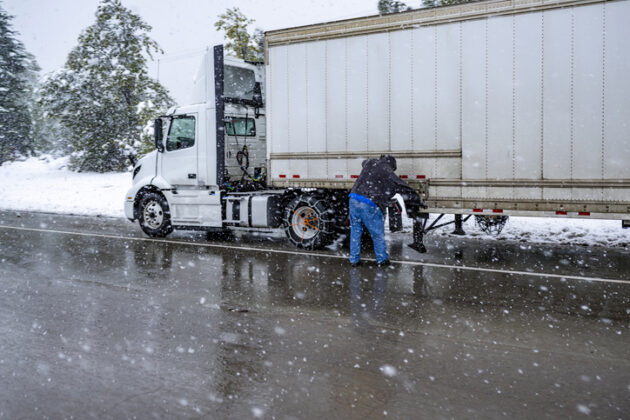 Experienced Truck driver puts chains on the wheels of the big rig semi truck with semi trailer to drive safely on a winter highway during a snow storm in the Lake Shasta region in California