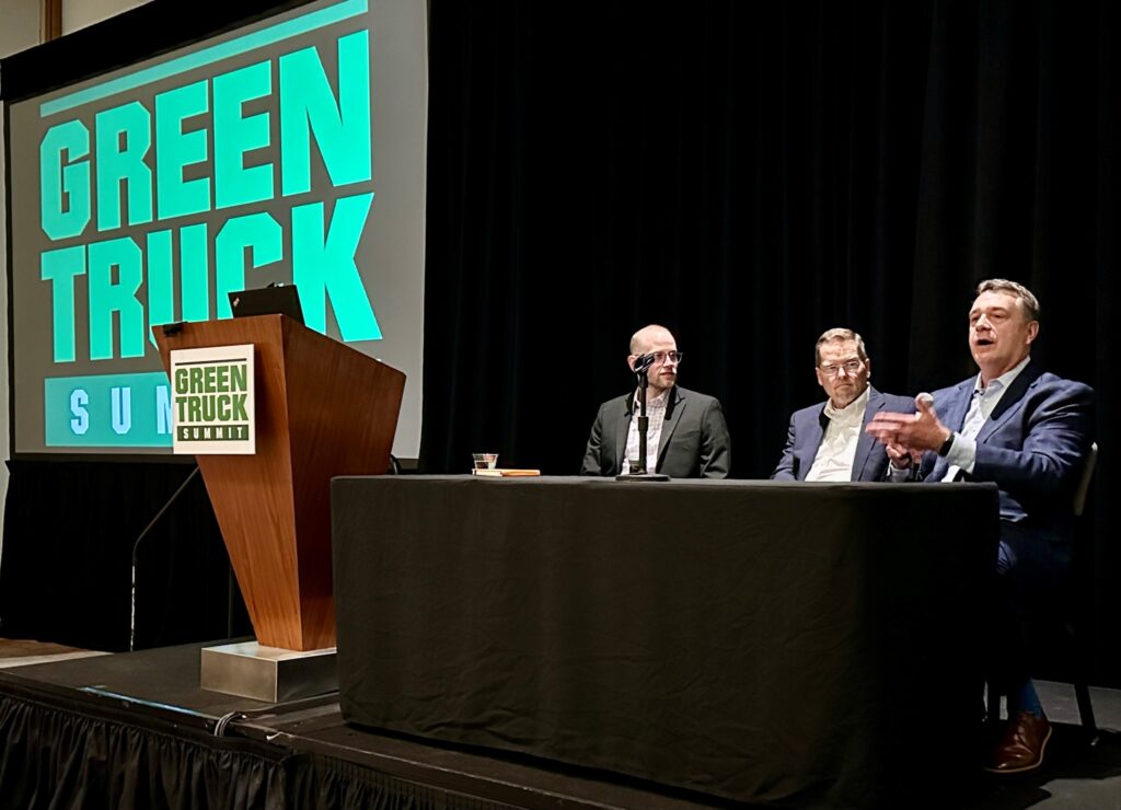 Three men seated on a stage