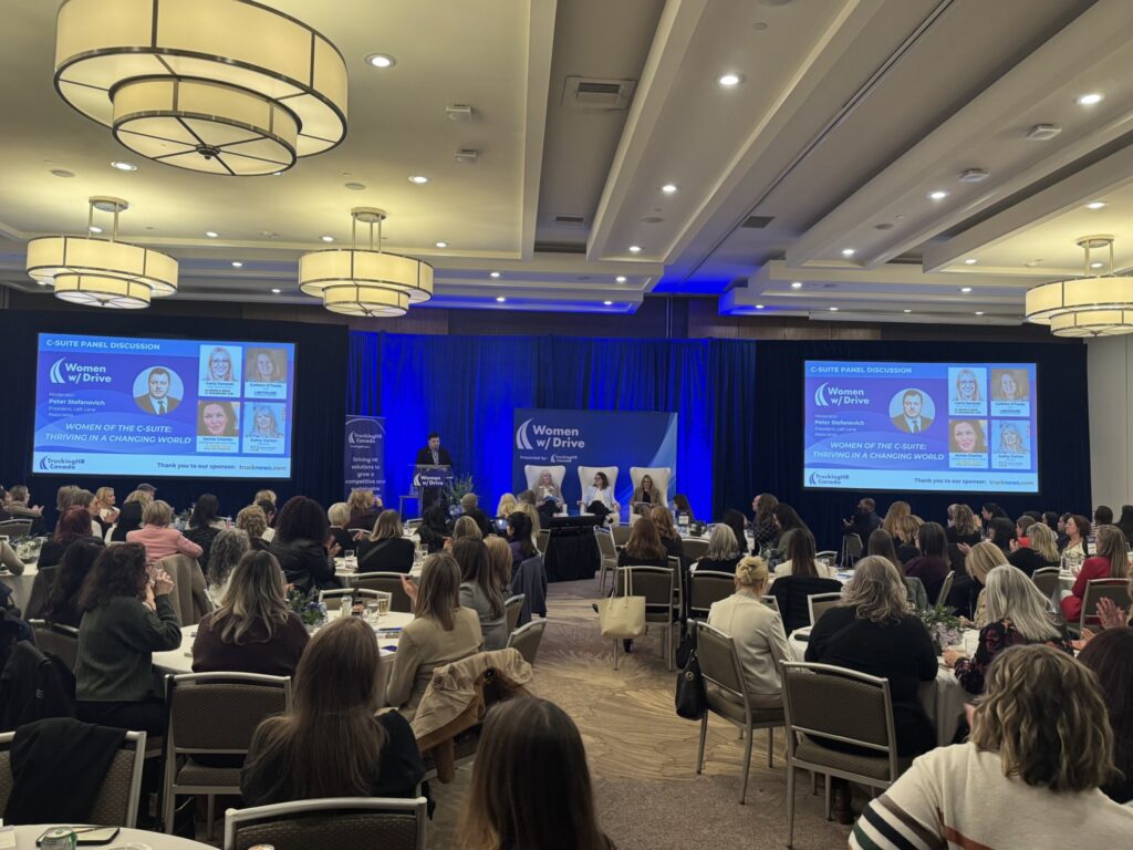 Three panelists and moderator on stage of WWD conference in front of a big audience