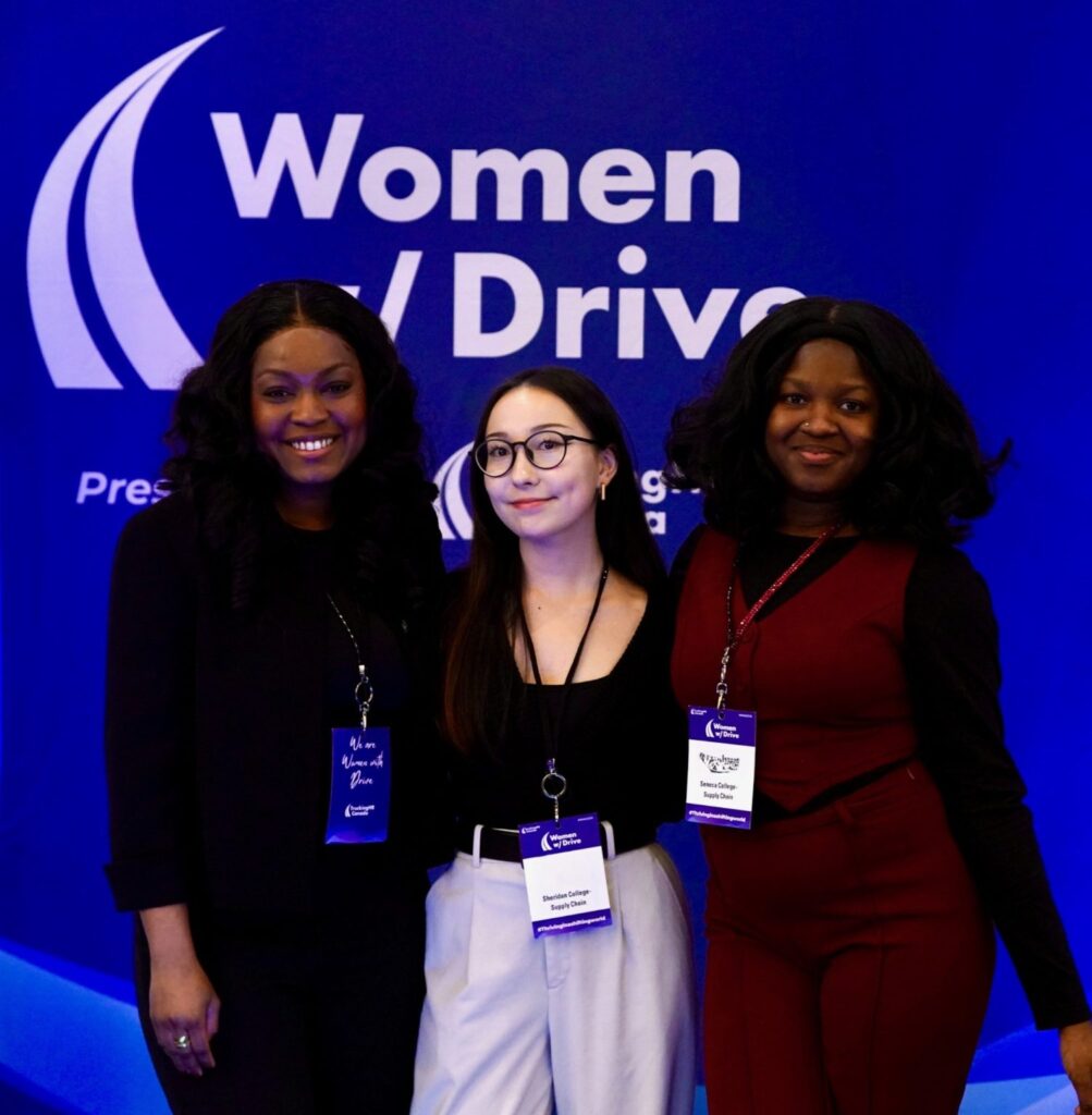Three female students in front of a Women with Drive banner
