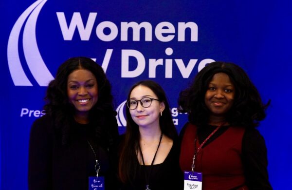 Three female students in front of a Women with Drive banner