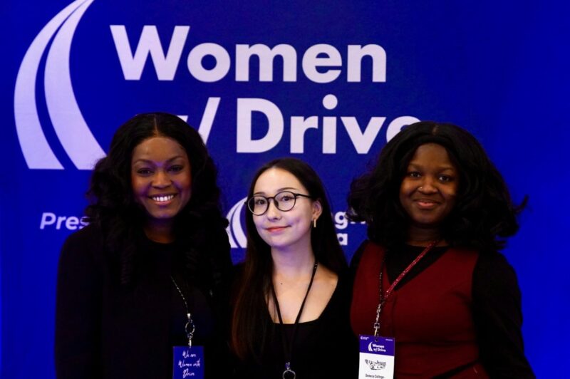 Three female students in front of a Women with Drive banner