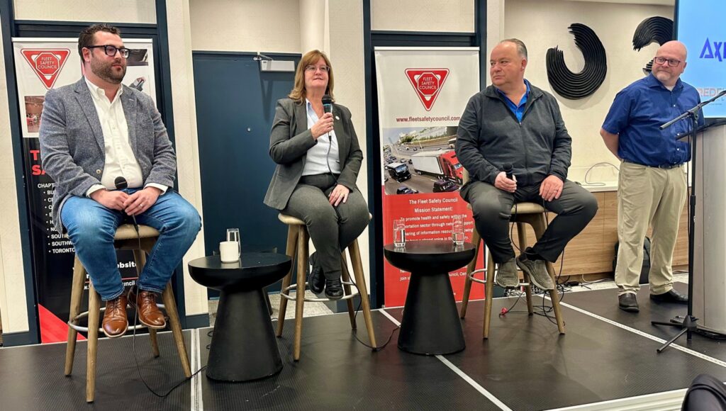 Three people seated and one standing on a stage
