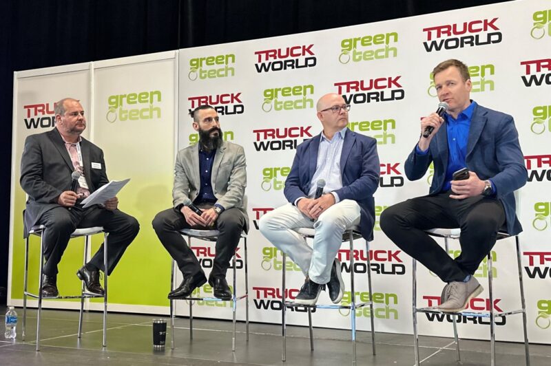 Four men sitting on stools on a stage