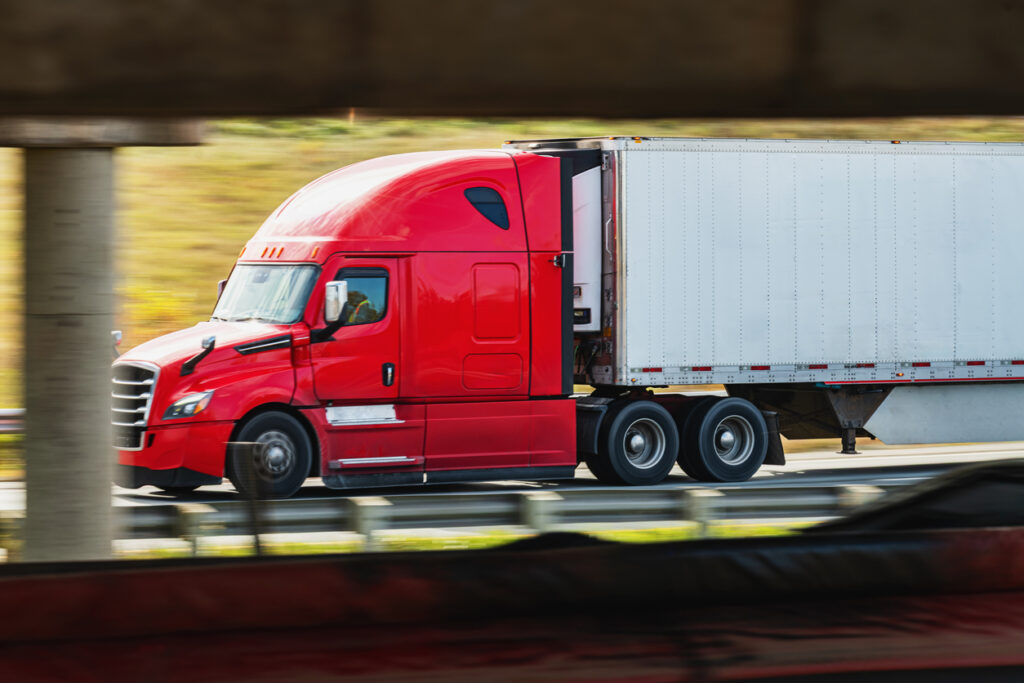A semi truck passes beneath a highway overpass in Canada. Panning shot with motion blur.