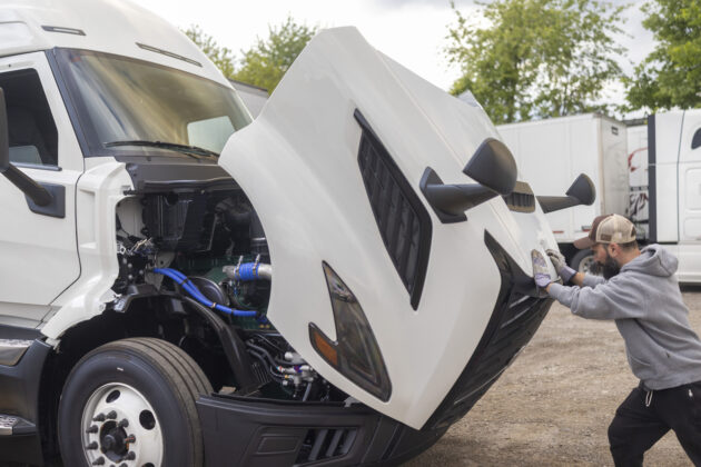 Bearded mechanic closing the hood of a white semi truck alternate text for this image