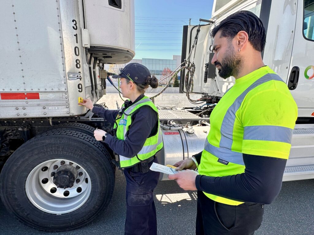Driver and MTO officer affixing a CVSA decal on a trailer